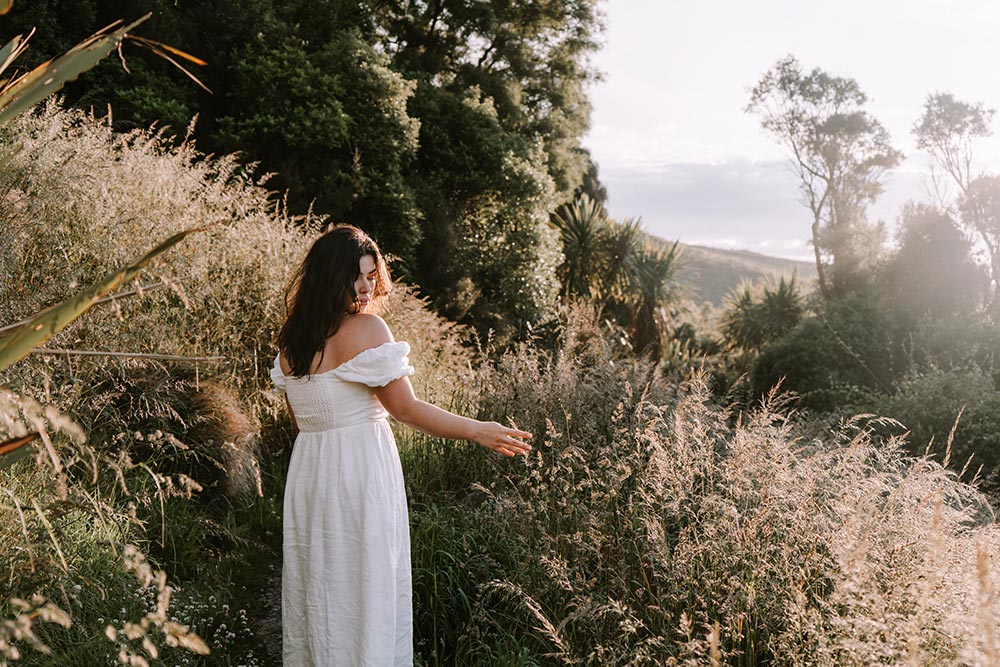 Woman in white dress walking through grassy sunlit pathway
